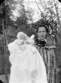 ouvrir dans la visionneuse : Suisse, femme portant dans ses bras un enfant en tenue de baptême.